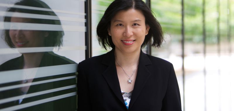 Exciton Science Associate Investigator Anita Ho-Baillie faces the camera and smiles while standing in front of a glass window and wearing a black blazer.