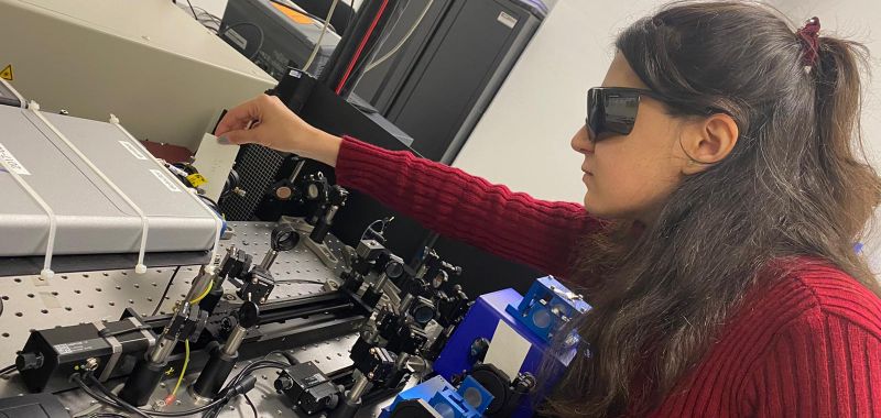 Dr Elham Gholizadeh, wearing a red jumper and black protective goggles, working with spectroscopy equipment in a laboratory at UNSW Sydney