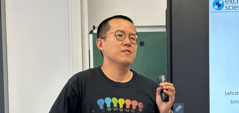 Heyou Zhang is wearing glasses and a black t-shirt during a presentation