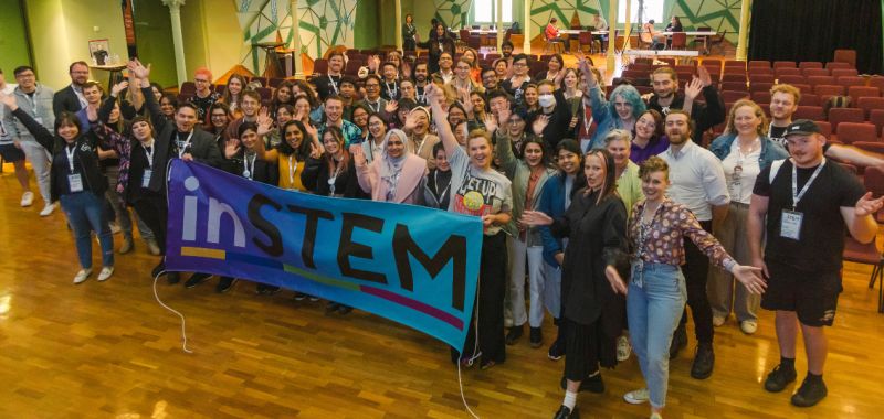 A group of people hold an inSTEM banner in RMIT's Storey Hall