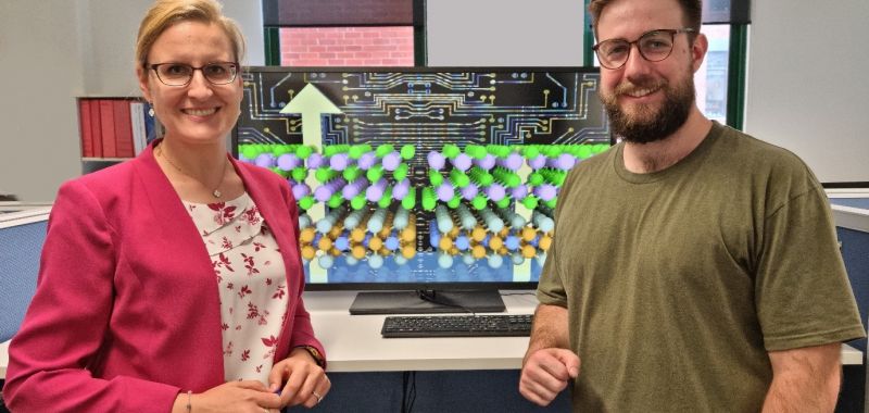Michelle Spencer (left) and Patrick Taylor (right) face the camera while standing in front a computer monitor displaying a graphical rendering of their research