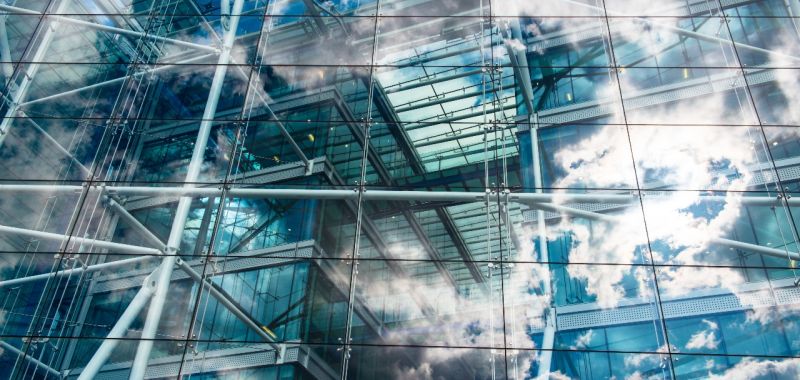 The glass windows of a modern building showing clouds and blue sky in their reflection