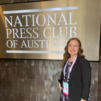 Alison Goldingay smiling at the camera in front of a sign that reads National Press Club of Australia