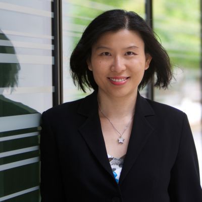Exciton Science Associate Investigator Anita Ho-Baillie faces the camera and smiles while standing in front of a glass window and wearing a black blazer.