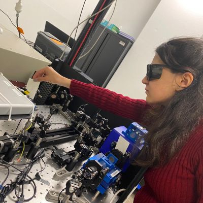 Dr Elham Gholizadeh, wearing a red jumper and black protective goggles, working with spectroscopy equipment in a laboratory at UNSW Sydney