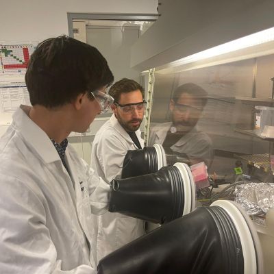 Sebastian Furer and Philippe Holzhey wearing labcoats and working in a nitrogen glovebox at Monash University