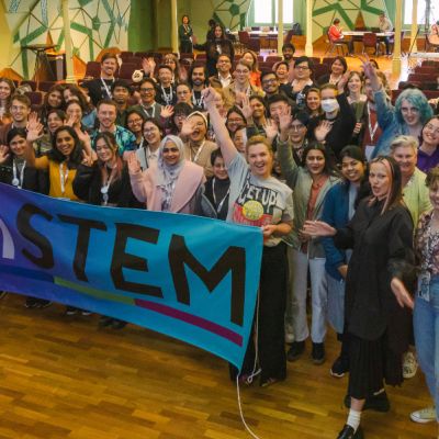 A group of people hold an inSTEM banner in RMIT's Storey Hall