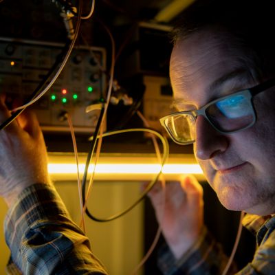 Dr Jamie Laird is pictured wearing glasses and operating an electronic device in a laser lab