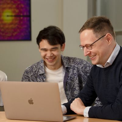 Ivan Kassal (right) sitting and smiling with two students while looking at a laptop
