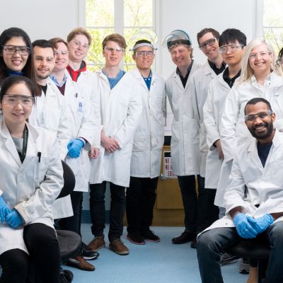 Members of the Nanoscience Lab at the University of Melbourne's School of Chemistry pose for a picture wearing white lab coats and clear plastic safety goggles