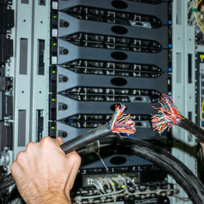 A pair of hands holding a severed cable in front of a computer server