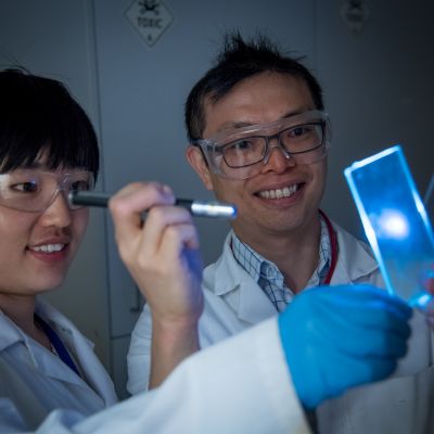 Wallace Wong (right) shining UV light on a sample with a student in a laboratory
