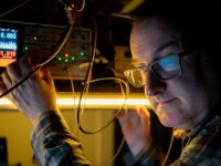 Dr Jamie Laird is pictured wearing glasses and operating an electronic device in a laser lab