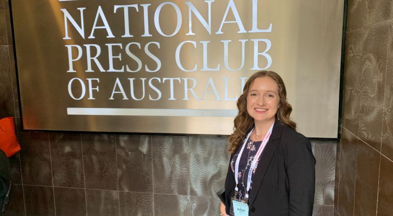 Alison Goldingay smiling at the camera in front of a sign that reads National Press Club of Australia