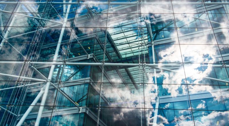 The glass windows of a modern building showing clouds and blue sky in their reflection